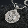 Load image into Gallery viewer, Polished silver Gemini zodiac pendant necklace on textured volcanic rock, centered macro jewelry photo with detailed horoscope twins relief and bright silver highlights.
