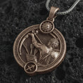 Load image into Gallery viewer, Bronze Sagittarius zodiac pendant necklace on textured volcanic rock, close-up studio shot highlighting the archer figure, bow and arrow, sun detail, and antique silver contrast.
