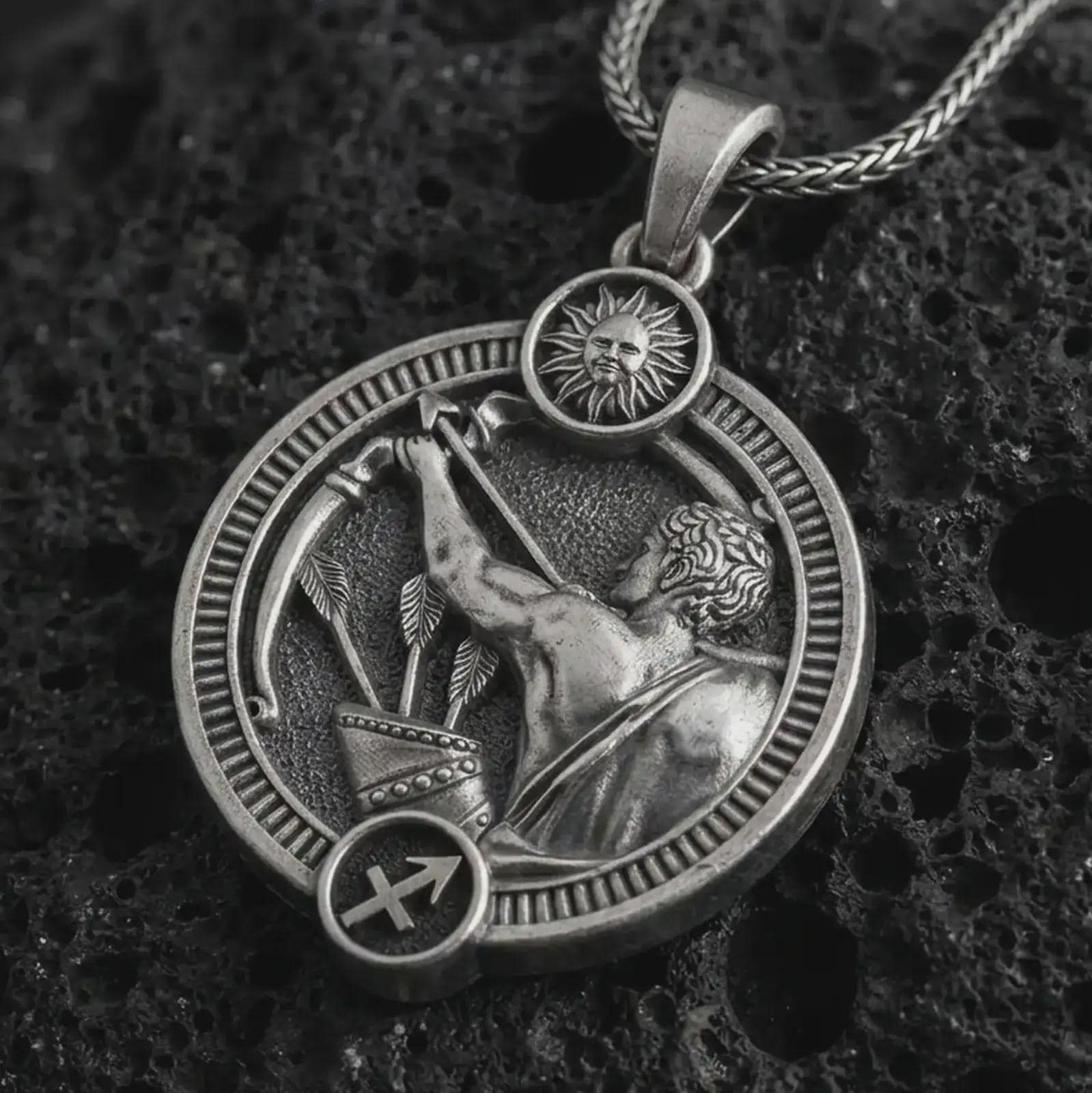 Oxidized Sagittarius zodiac pendant necklace on textured volcanic rock, close-up studio shot highlighting the archer figure, bow and arrow, sun detail, and antique silver contrast.
