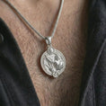 Load image into Gallery viewer, Polished silver Sagittarius zodiac pendant necklace worn on the chest, masculine lifestyle shot highlighting the bow and arrow relief, sun detail, and bright silver finish.
