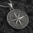 Load image into Gallery viewer, Oxidized compass rose pendant necklace on textured volcanic rock, close-up studio shot highlighting the raised directional star, cardinal letters, circular map dial, and antique silver contrast.
