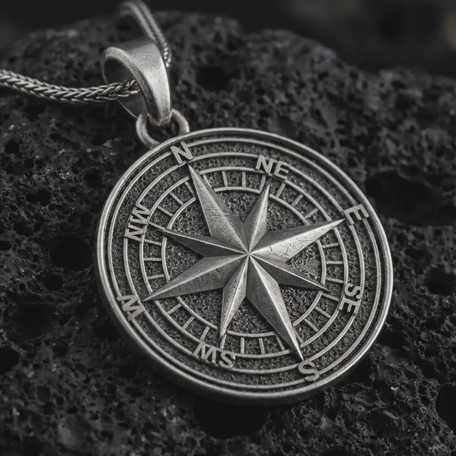 Oxidized compass rose pendant necklace on textured volcanic rock, close-up studio shot highlighting the raised directional star, cardinal letters, circular map dial, and antique silver contrast.