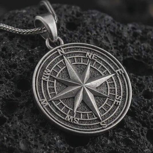 Oxidized compass rose pendant necklace on textured volcanic rock, close-up studio shot highlighting the raised directional star, cardinal letters, circular map dial, and antique silver contrast.
