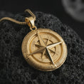 Load image into Gallery viewer, Gold plated compass pendant necklace on textured volcanic rock, premium close-up studio composition emphasizing the nautical amulet design, cardinal directions, and explorer symbolism.
