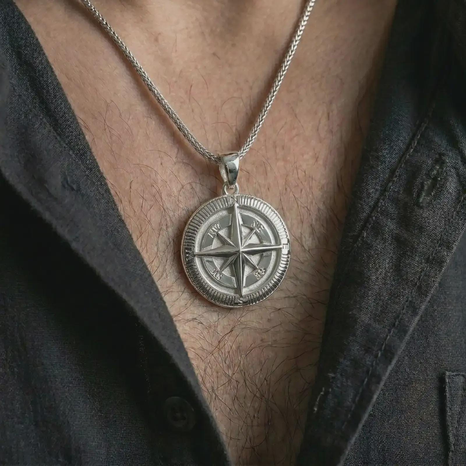 Polished silver compass pendant necklace worn on the chest, masculine lifestyle shot highlighting the bright silver finish, raised compass star, and directional letter details.