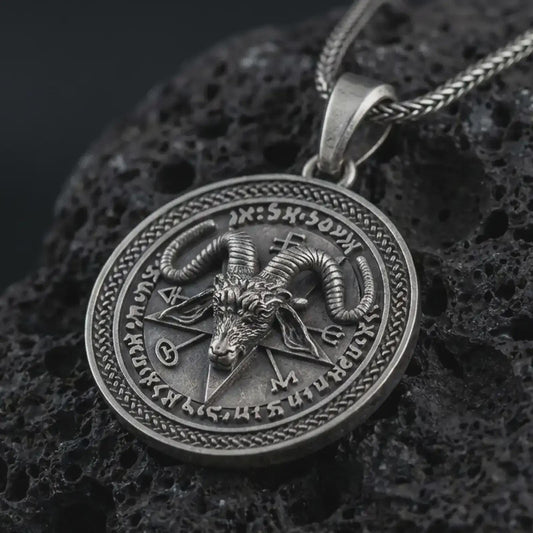 Oxidized Baphomet pendant necklace on textured volcanic rock, close-up studio shot highlighting the goat head relief, pentagram background, occult sigils, and antique silver contrast.