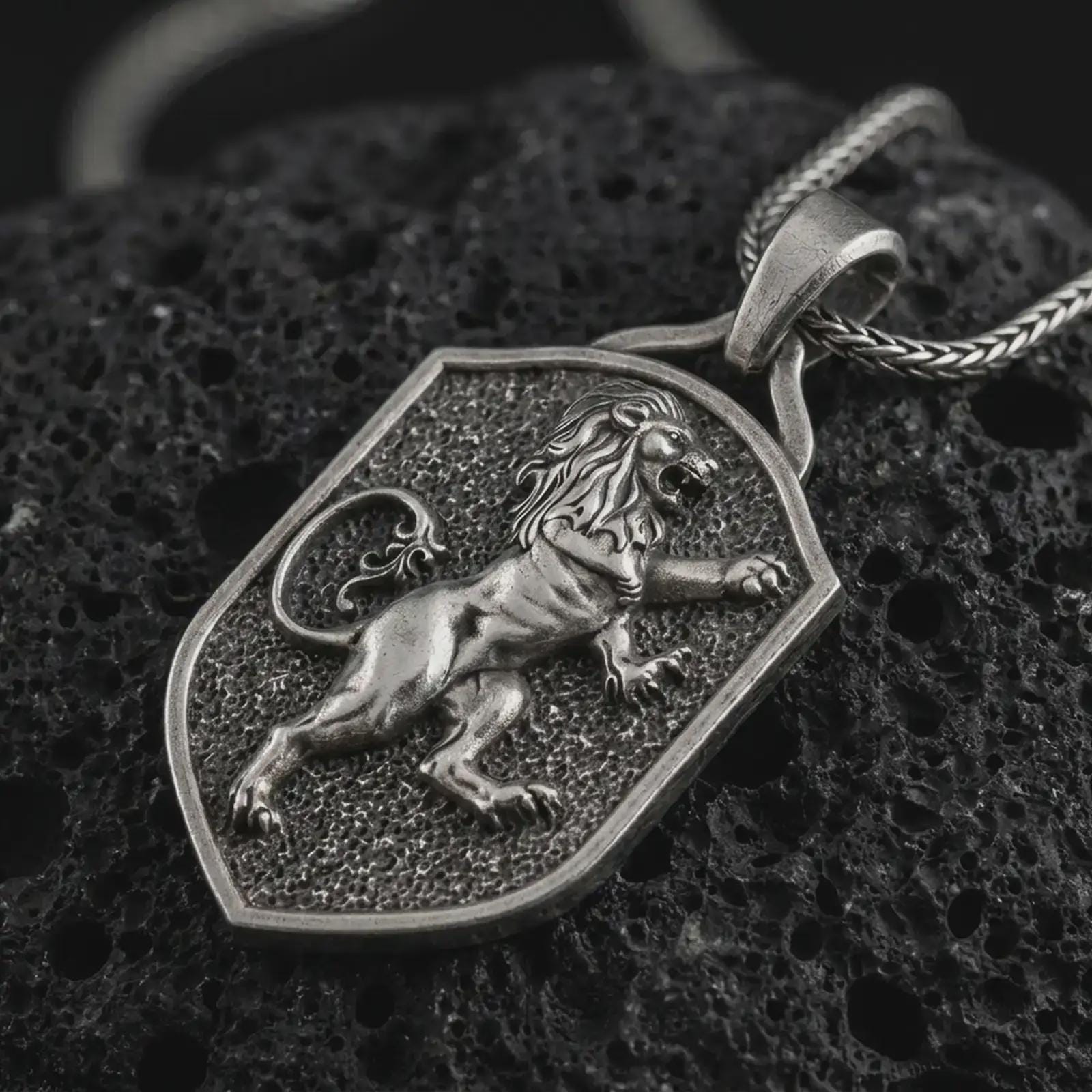 Oxidized heraldic lion shield pendant necklace on textured volcanic rock, close-up studio shot highlighting the rampant lion relief, shield frame, textured background, and antique silver contrast.
