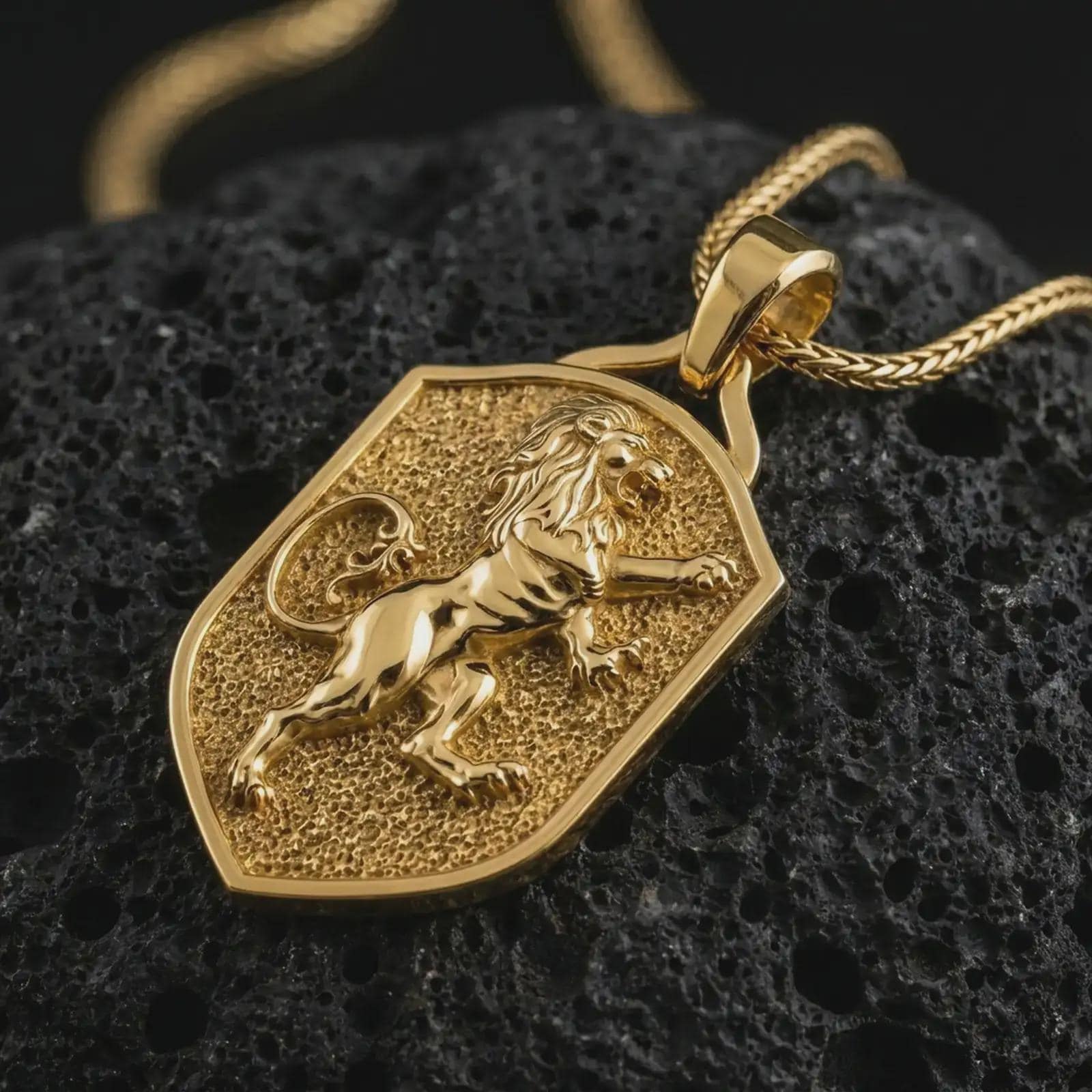 Gold plated heraldic lion shield pendant necklace on textured volcanic rock, premium close-up studio composition emphasizing the royal rampant lion, medieval shield shape, and noble crest design.