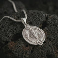 Load image into Gallery viewer, Polished silver Capricorn zodiac pendant necklace on textured volcanic rock, centered macro jewelry photo with detailed sea goat horoscope relief and bright silver highlights.
