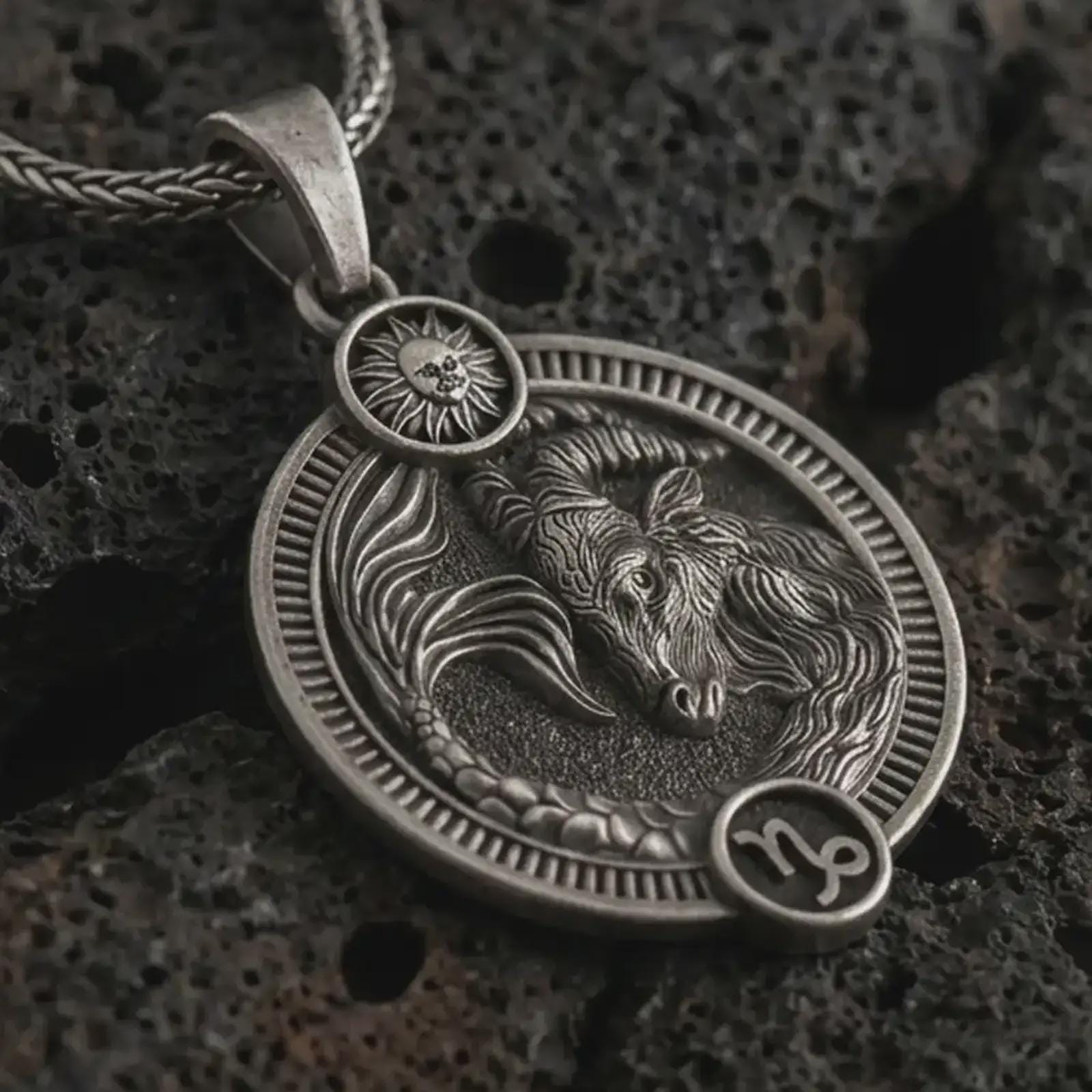 Oxidized Capricorn zodiac pendant necklace on textured volcanic rock, close-up studio shot highlighting the sea goat relief, sun detail, Capricorn symbol, and antique silver contrast.