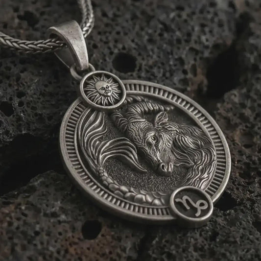 Oxidized Capricorn zodiac pendant necklace on textured volcanic rock, close-up studio shot highlighting the sea goat relief, sun detail, Capricorn symbol, and antique silver contrast.