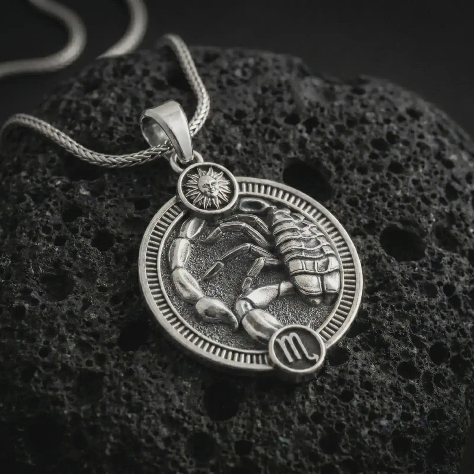 Polished silver Scorpio zodiac pendant necklace on textured volcanic rock, centered macro jewelry photo with detailed scorpion horoscope relief and bright silver highlights.