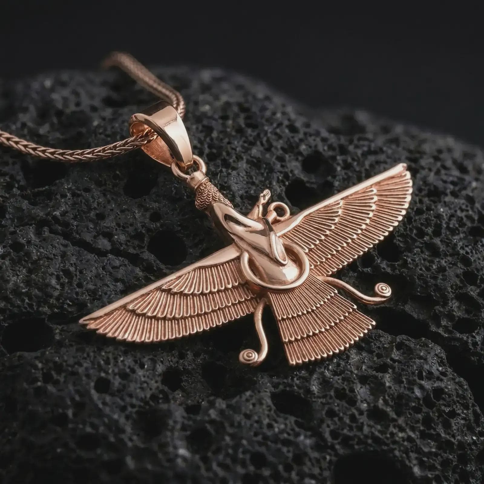 Rose gold plated Faravahar pendant necklace on textured volcanic rock, detailed macro product shot with soft warm reflections and symbolic Zoroastrian styling.