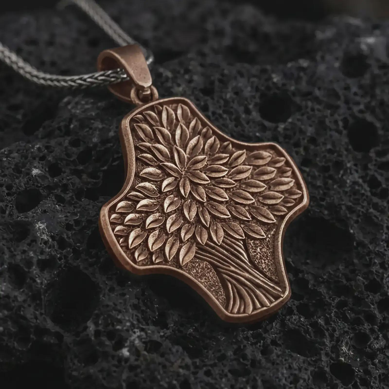 An Bronze Tree of Life cross pendant rests on dark volcanic rock in a macro studio close-up, showing layered leaf details and an organic botanical shape.