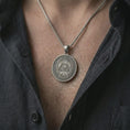 Load image into Gallery viewer, Oxidized all-seeing eye pendant necklace worn on the chest, close-up lifestyle jewelry photo showing the symbolic eye medallion on a spiga chain with dark clothing.
