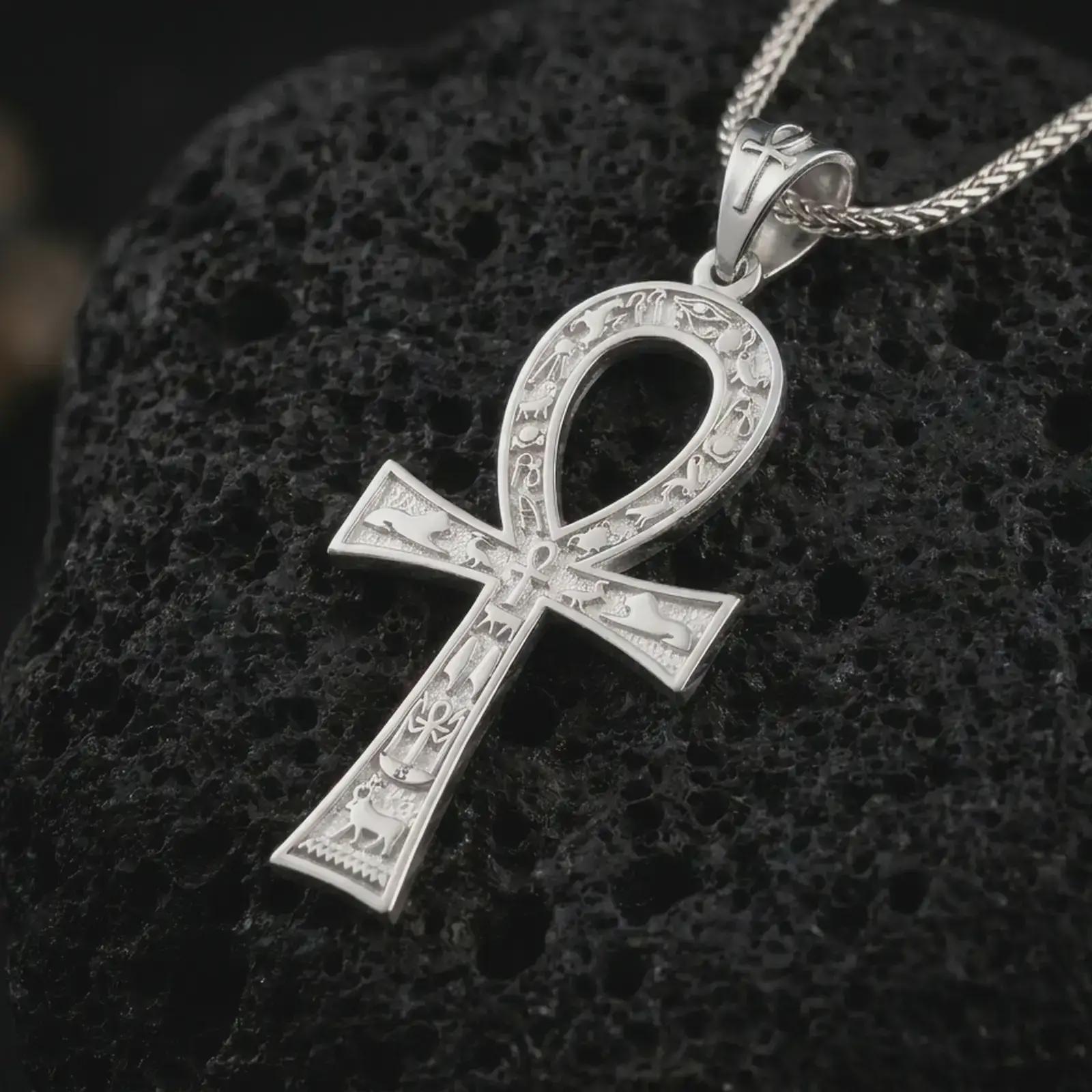 Polished silver ankh cross pendant necklace on textured volcanic rock, centered macro jewelry photo with detailed Egyptian engravings, open loop shape, and bright silver highlights.
