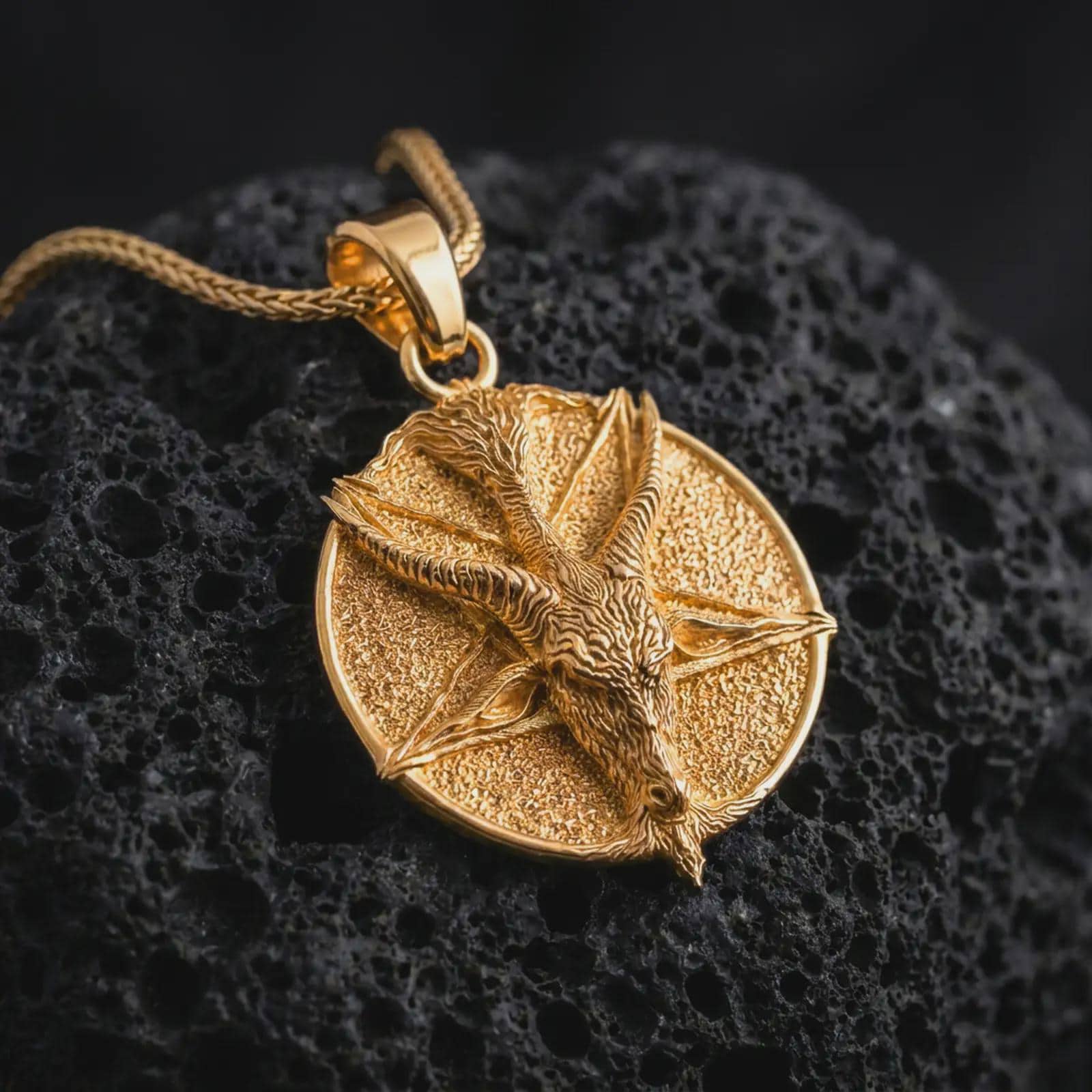 Gold plated goat pentagram pendant necklace on textured volcanic rock, premium close-up studio composition emphasizing the occult goat figure, pentagram symbol, and dark gothic amulet design.