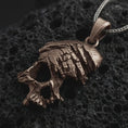 Load image into Gallery viewer, Bronze cracked skull pendant necklace on textured volcanic rock, close-up studio shot highlighting the fractured skull form, deep cut details, gothic texture, and antique silver contrast.
