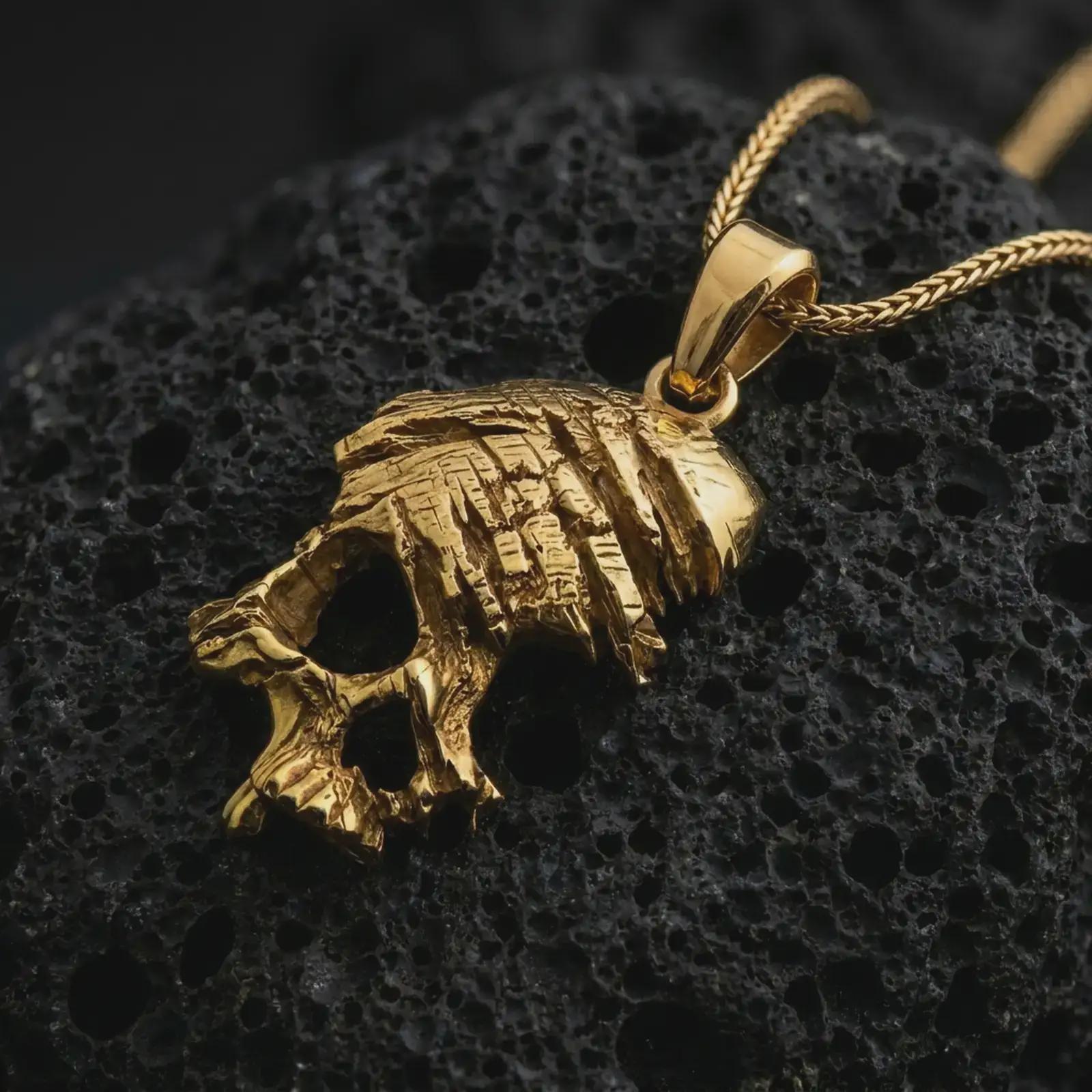 Gold plated cracked skull pendant necklace on textured volcanic rock, premium close-up studio composition emphasizing the edgy skull silhouette, jagged cracks, and dark punk jewelry design.