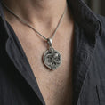 Load image into Gallery viewer, Oxidized Aquarius zodiac pendant necklace worn on the chest, close-up lifestyle jewelry photo showing the astrology medallion on a spiga chain with dark clothing.
