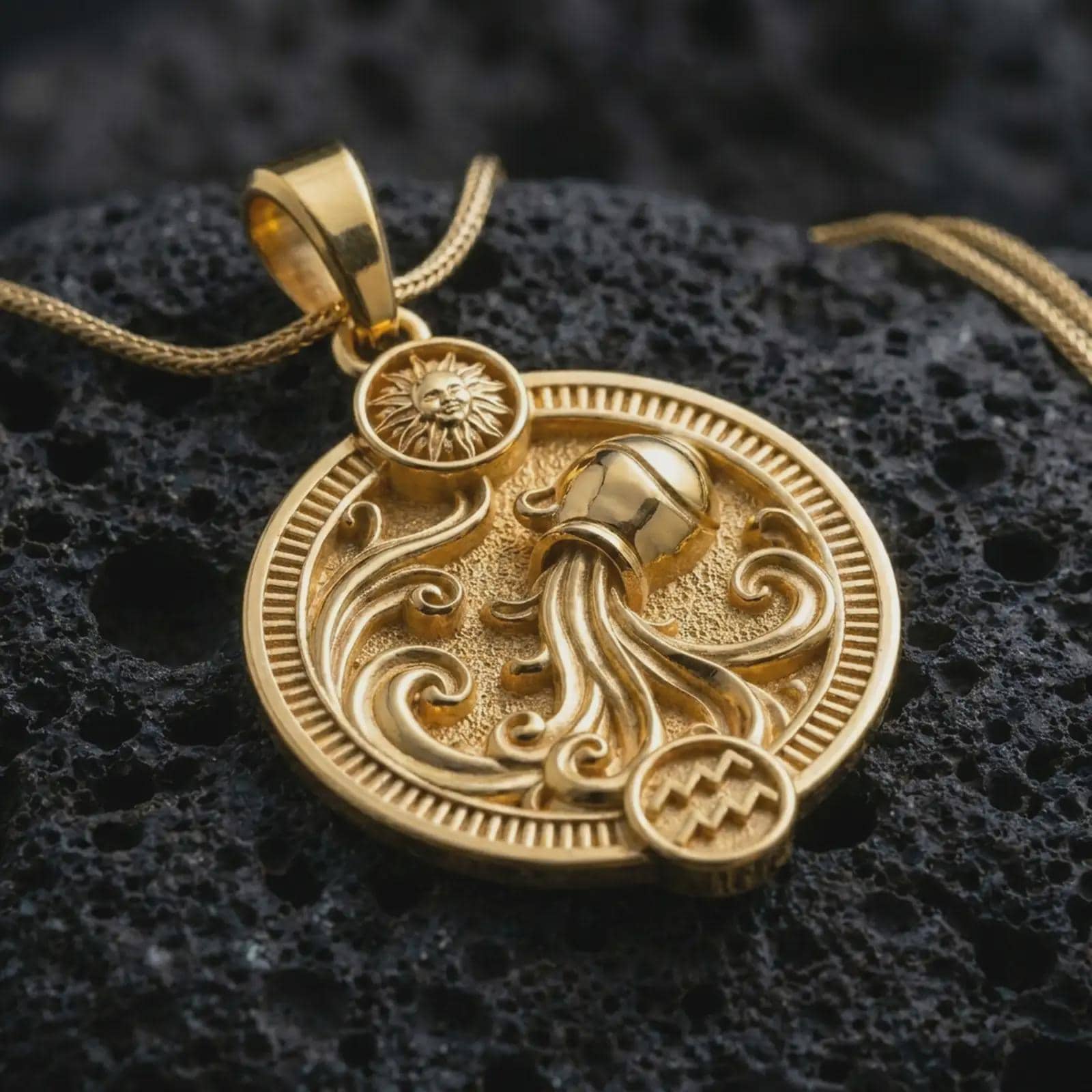 Gold plated Aquarius zodiac pendant necklace on textured volcanic rock, premium close-up studio composition emphasizing the flowing water motif, sun charm, and astrology medallion design.