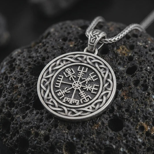 Oxidized Vegvisir Viking compass pendant necklace on textured volcanic rock, close-up studio shot highlighting the Norse protection symbol, Celtic knot border, and antique silver contrast.