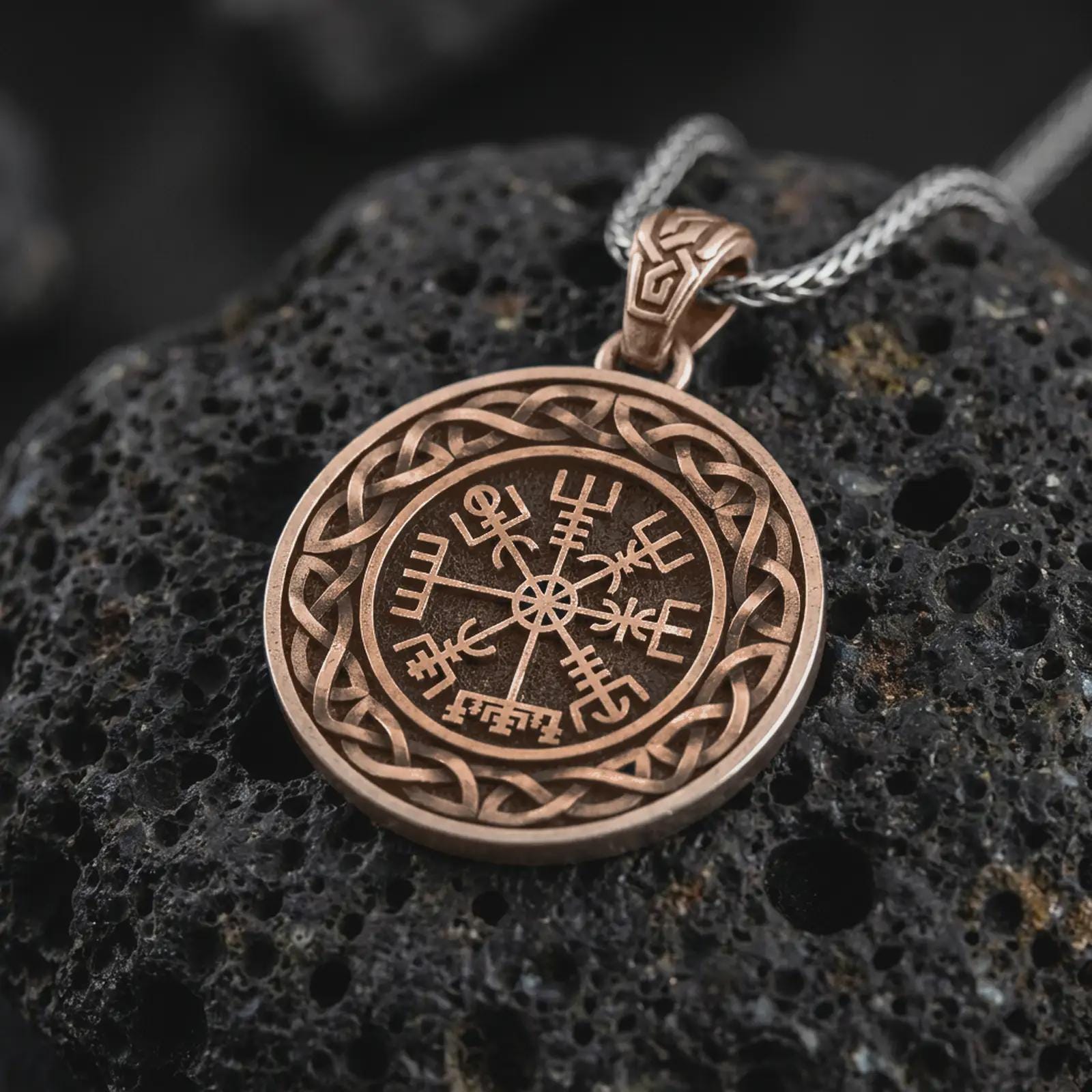 Bronze Vegvisir Viking compass pendant necklace on textured volcanic rock, close-up studio shot highlighting the Norse protection symbol, Celtic knot border, and antique silver contrast.