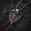 Load image into Gallery viewer, Bronze biomechanical ram skull pendant necklace on textured volcanic rock, close-up studio shot highlighting the curved horns, skeletal ram face, cyber gothic details, and antique silver contrast.
