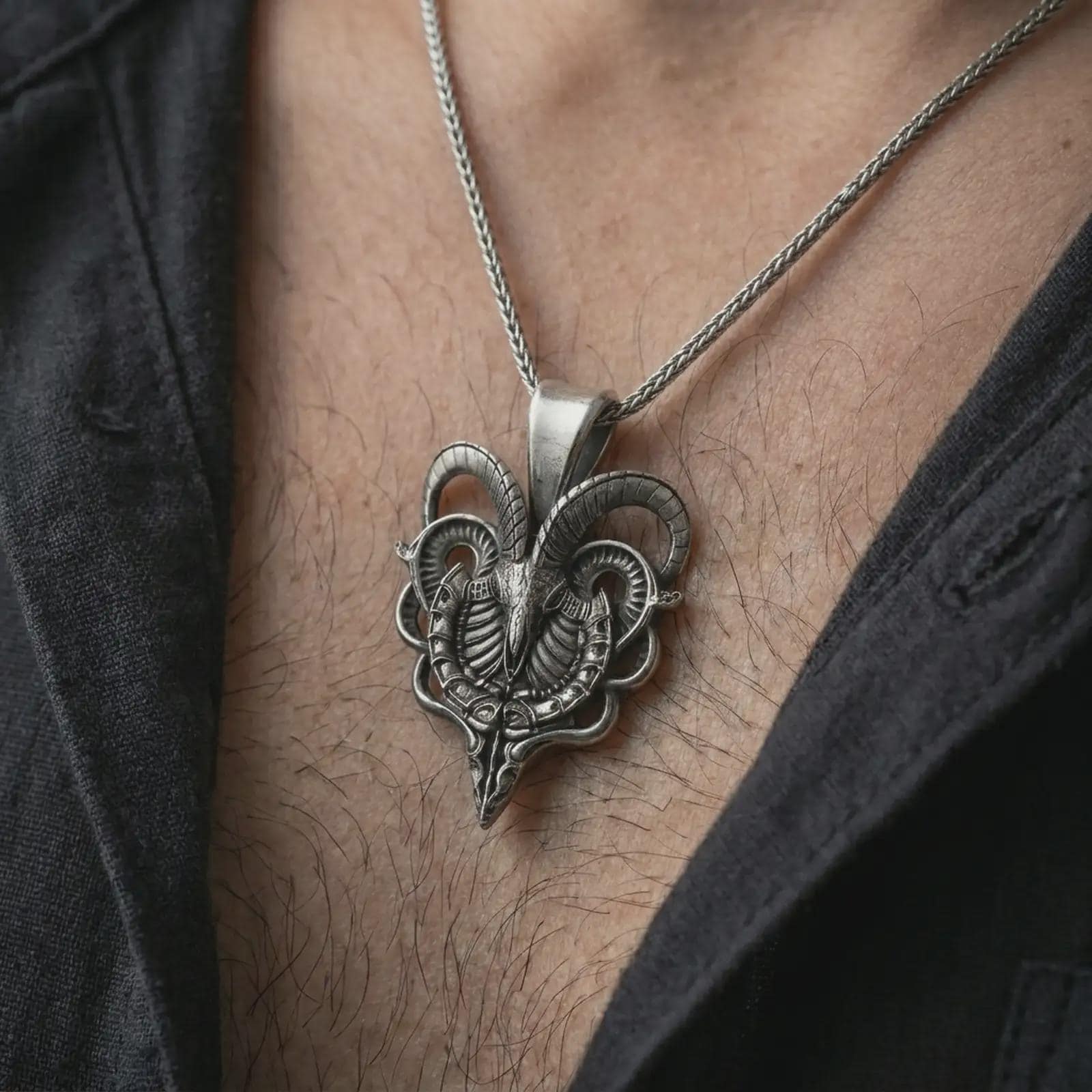 Oxidized biomechanical ram skull pendant necklace worn on the chest, close-up lifestyle jewelry photo showing the cyber gothic ram pendant on a spiga chain with dark clothing.
