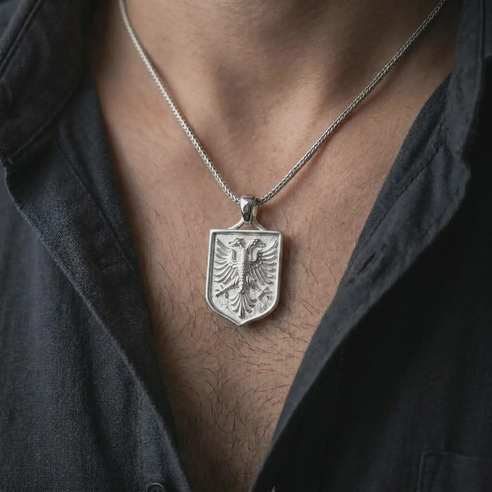Polished silver double-headed eagle shield pendant necklace worn on the chest, masculine lifestyle shot highlighting the twin eagle relief, shield frame, and bright silver finish.