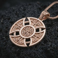 Load image into Gallery viewer, Rose gold plated Celtic cross pendant necklace on textured volcanic rock, detailed macro product shot with soft warm reflections and intricate Celtic knot symbolism.
