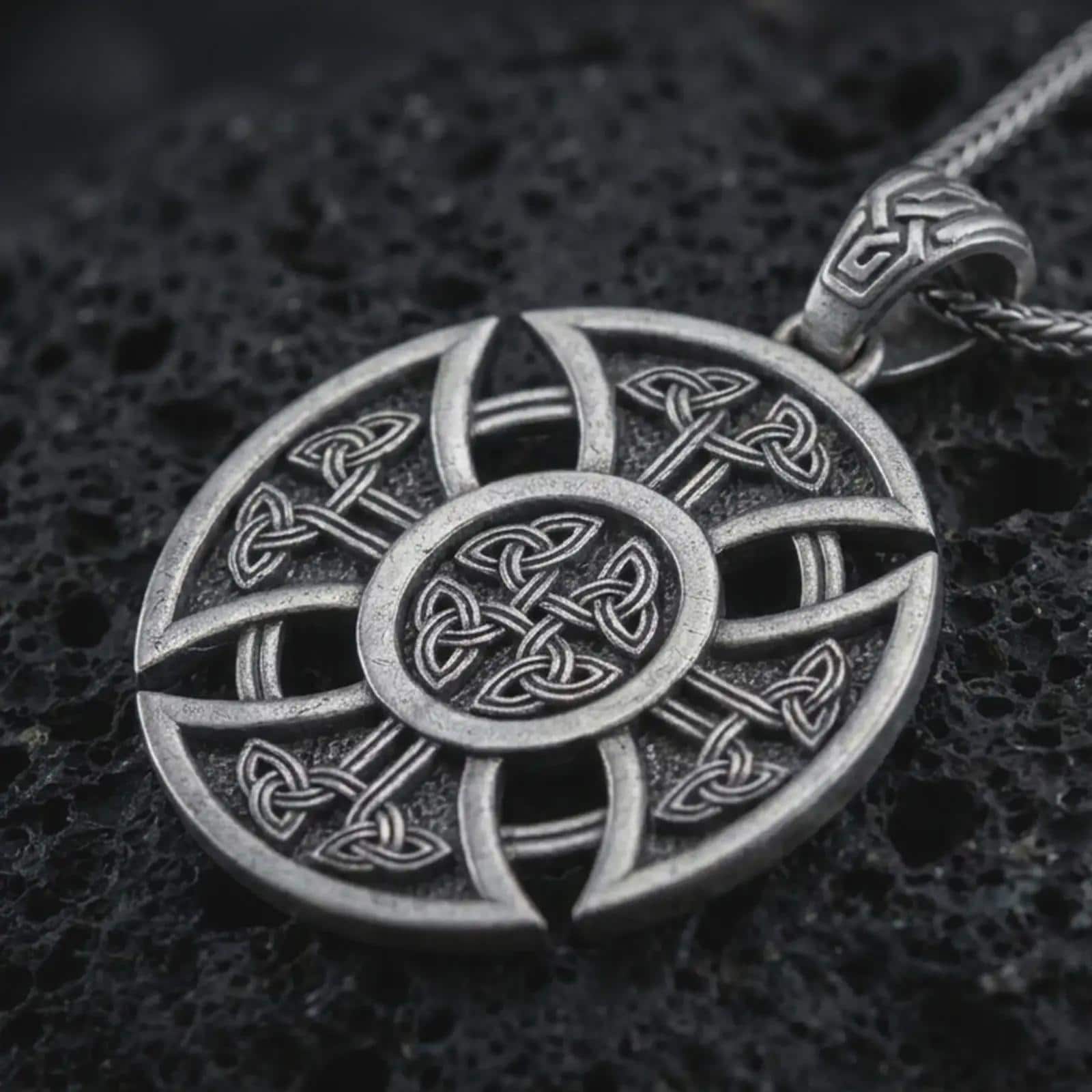 Oxidized Celtic cross pendant necklace on textured volcanic rock, close-up studio shot highlighting the circular cross shape, Norse knotwork pattern, openwork details, and antique silver contrast.