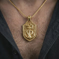 Load image into Gallery viewer, Gold plated serpent and anchor pendant necklace worn on the chest, premium lifestyle jewelry photo with the shield-shaped nautical pendant centered on a spiga chain.
