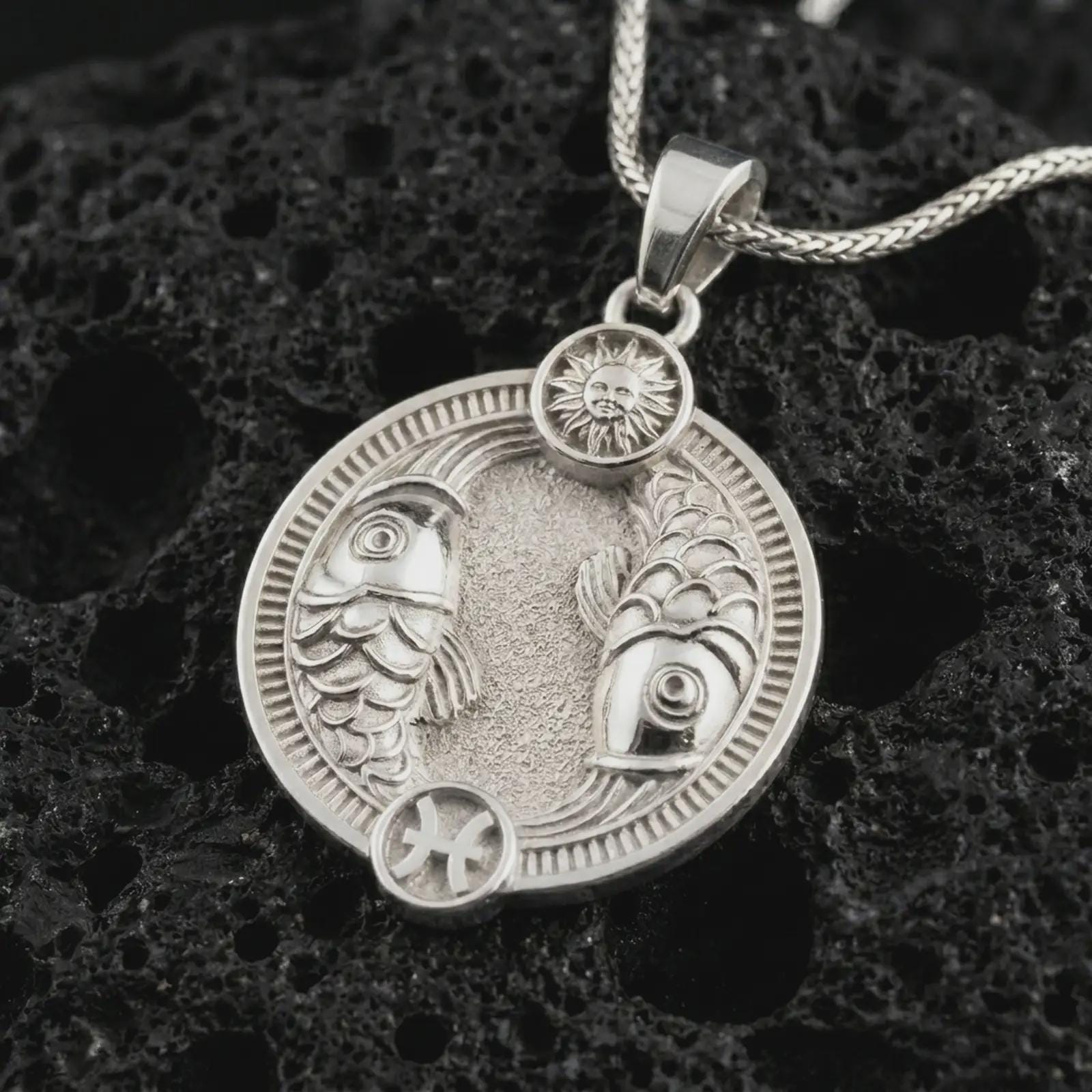 Polished silver Pisces zodiac pendant necklace on textured volcanic rock, centered macro jewelry photo with detailed twin fish relief and bright silver highlights.