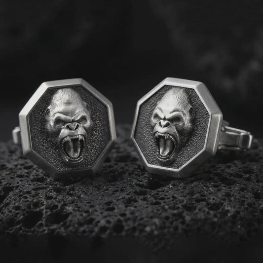 Oxidized gorilla cufflinks on textured volcanic rock, close-up studio shot highlighting the roaring ape face, octagonal frame, deep relief, and antique silver contrast.
