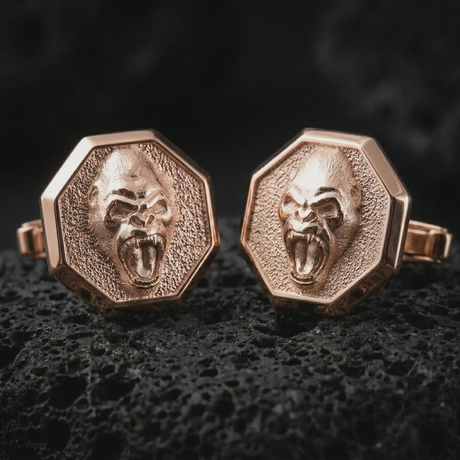 Rose gold plated gorilla cufflinks on textured volcanic rock, detailed macro product shot with soft warm reflections and powerful gorilla symbolism.