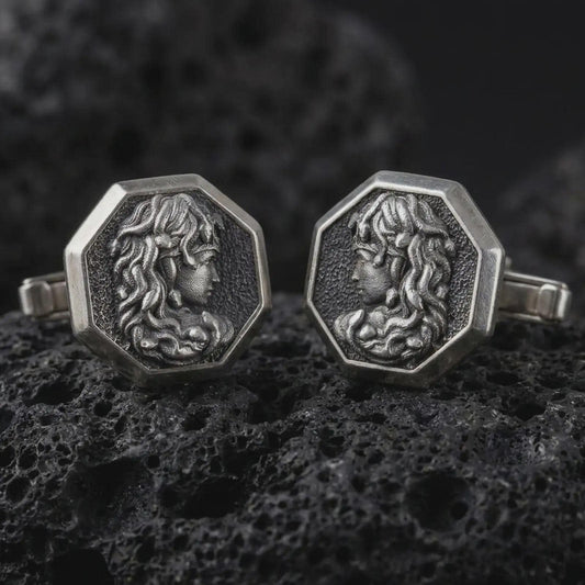 An oxidized Medusa cufflink pair rests on dark volcanic rock in a macro studio close-up, showing a sculpted Gorgon profile inside octagon frames.