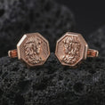 Load image into Gallery viewer, Rose gold plated Medusa cufflinks are photographed on porous volcanic rock in a close-up studio composition with refined luxury lighting.
