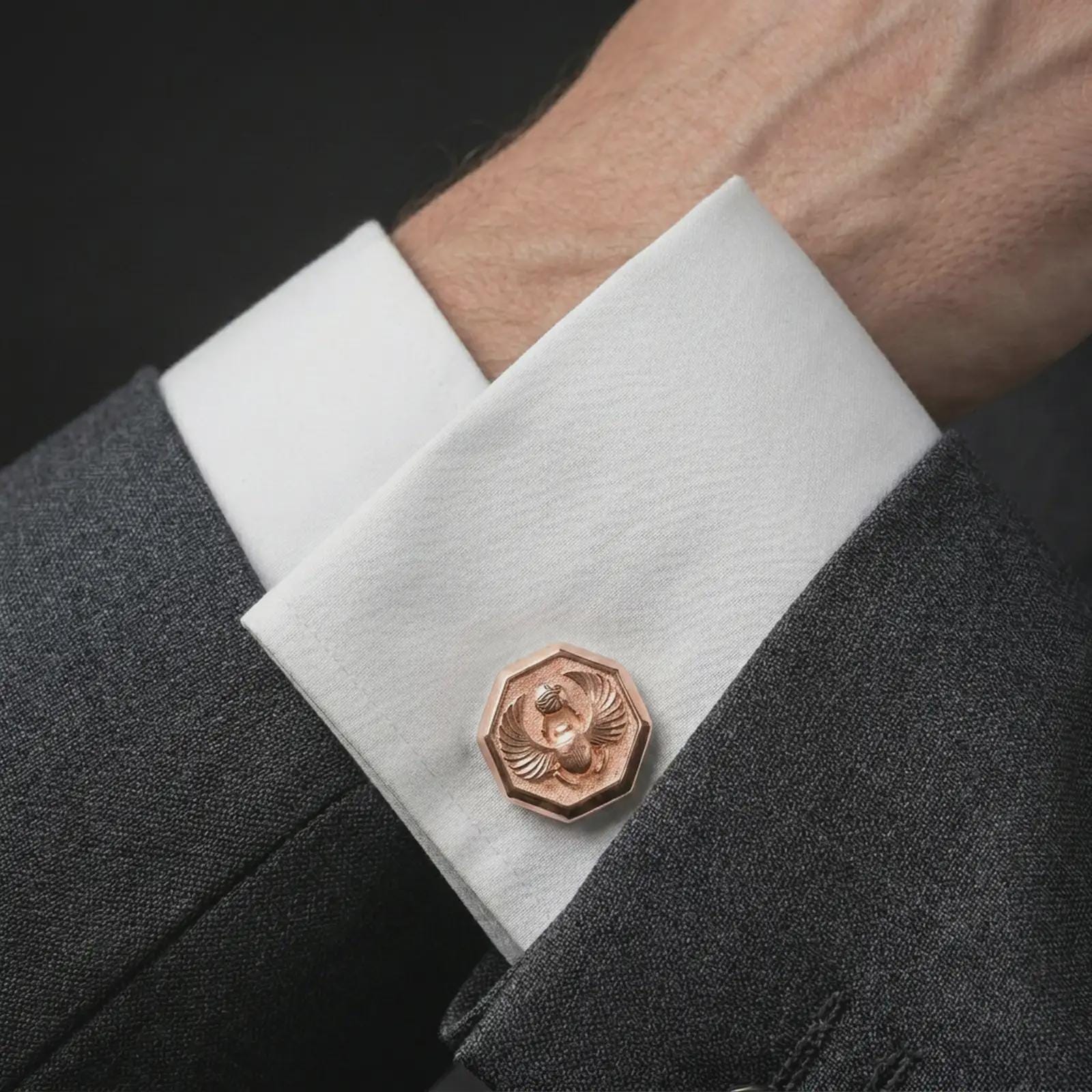 A rose gold plated scarab cufflink is worn on a shirt cuff in a close-up lifestyle composition, highlighting its octagon frame and scarab motif.