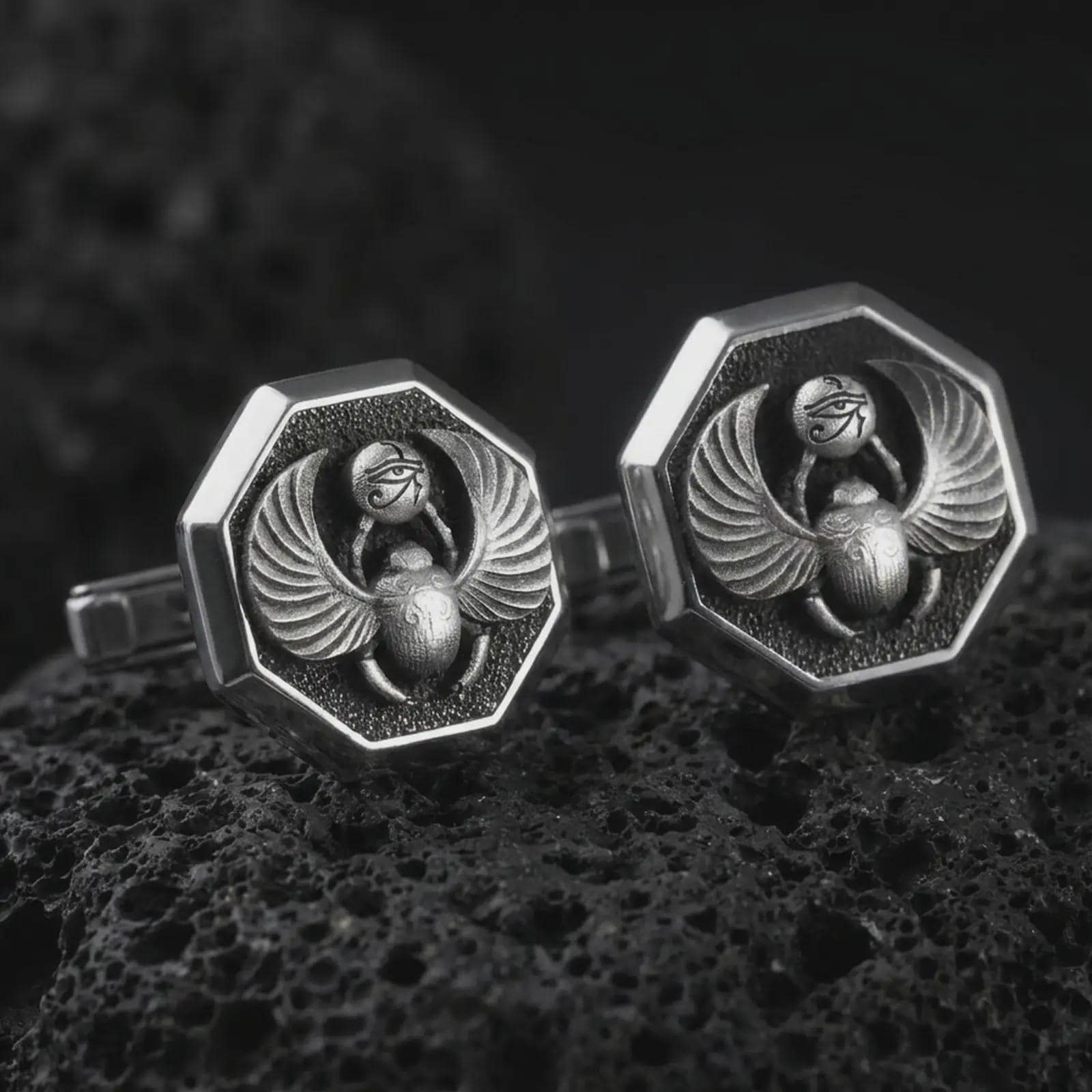 An oxidized scarab cufflink pair rests on dark volcanic rock in a macro studio close-up, showing winged beetle details and ancient Egyptian symbolism.