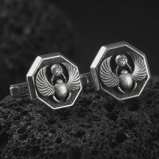 An oxidized scarab cufflink pair rests on dark volcanic rock in a macro studio close-up, showing winged beetle details and ancient Egyptian symbolism.