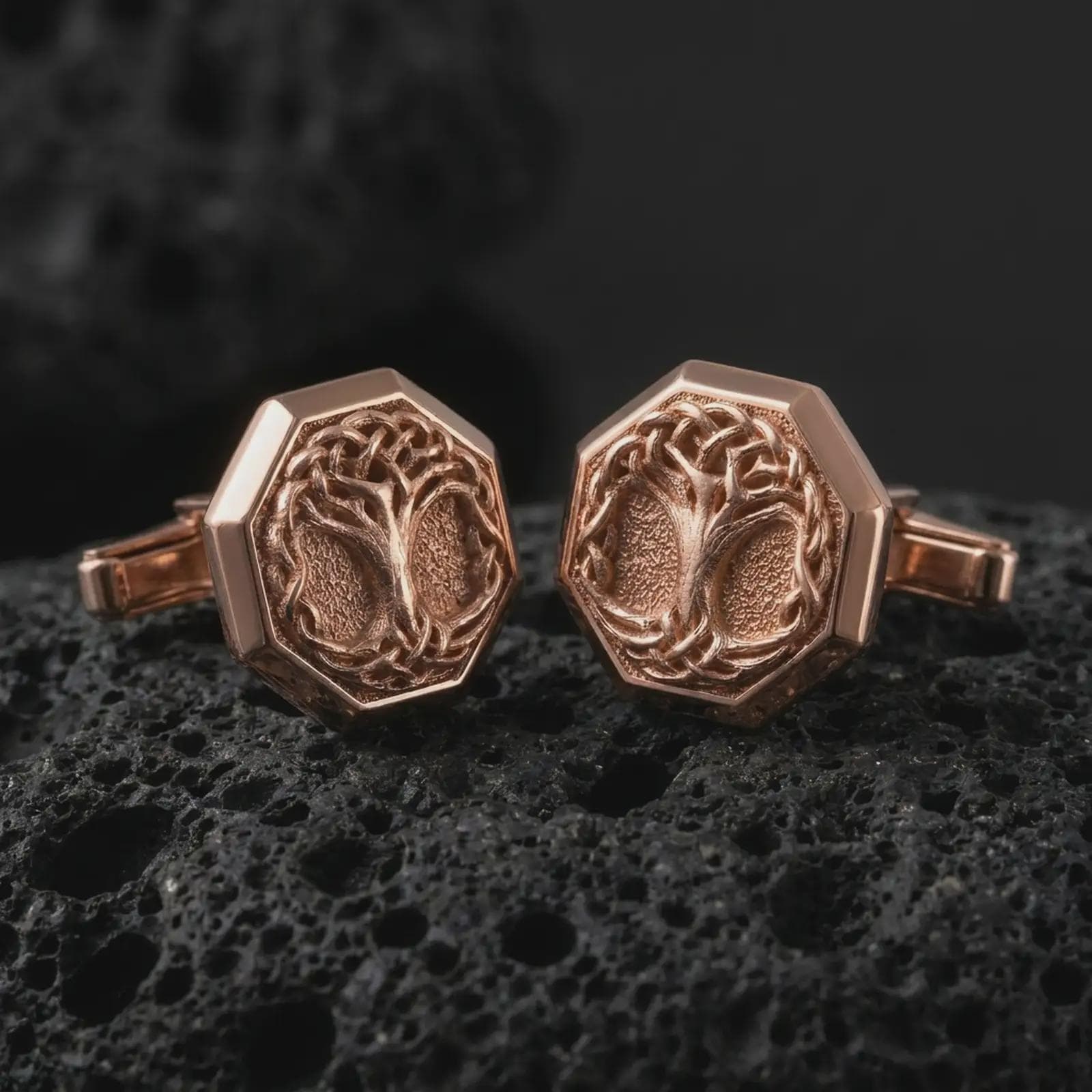 Rose gold plated Yggdrasil cufflinks are photographed on porous volcanic rock in a close-up studio composition with refined luxury lighting and symbolic branch detail.