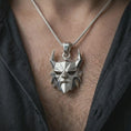 Load image into Gallery viewer, A polished silver Surtur pendant is worn on the neck in a premium close-up lifestyle image, showing the angular horned mask design clearly.
