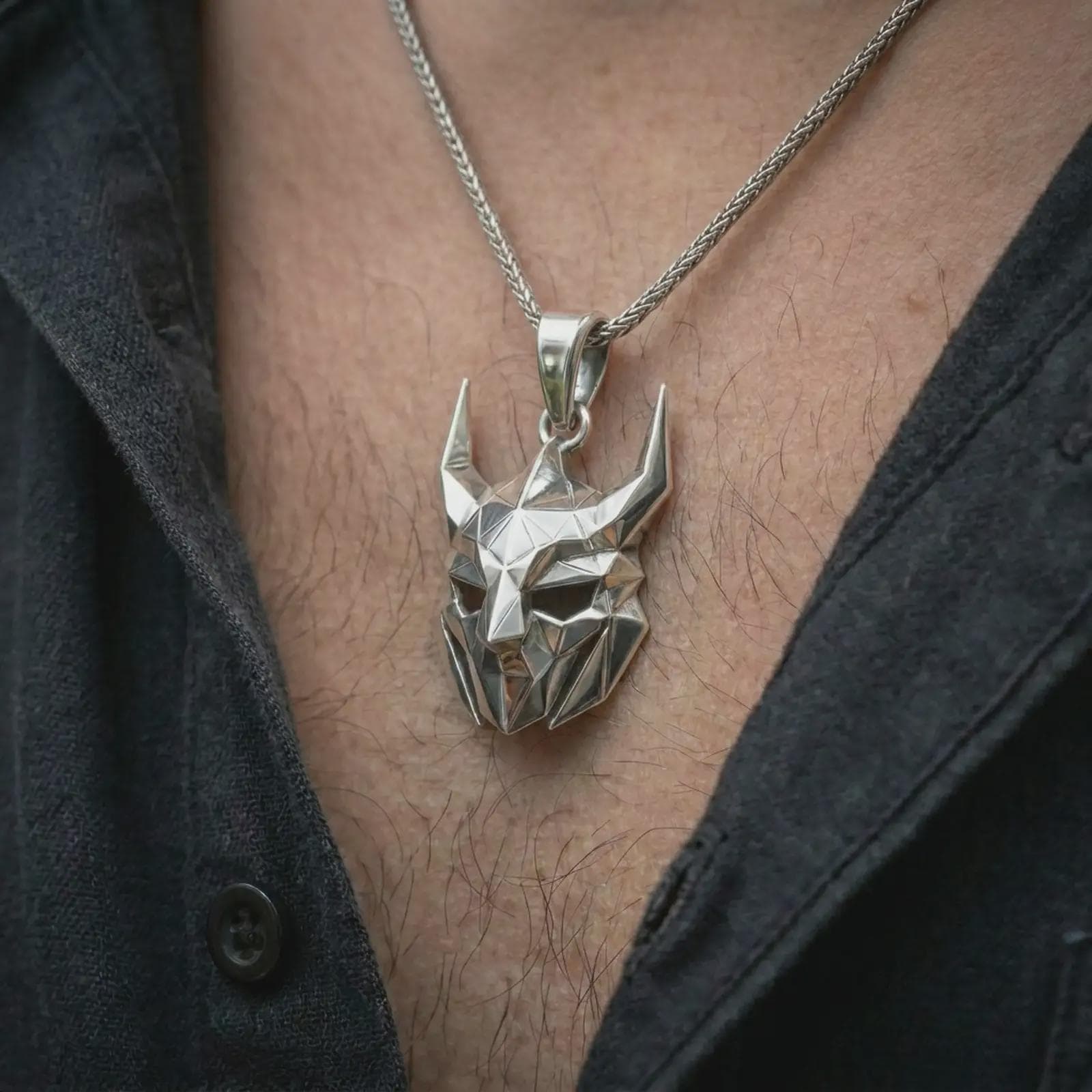 A polished silver Loki pendant is worn on the neck in a premium close-up lifestyle image, showing the faceted horned mask clearly.