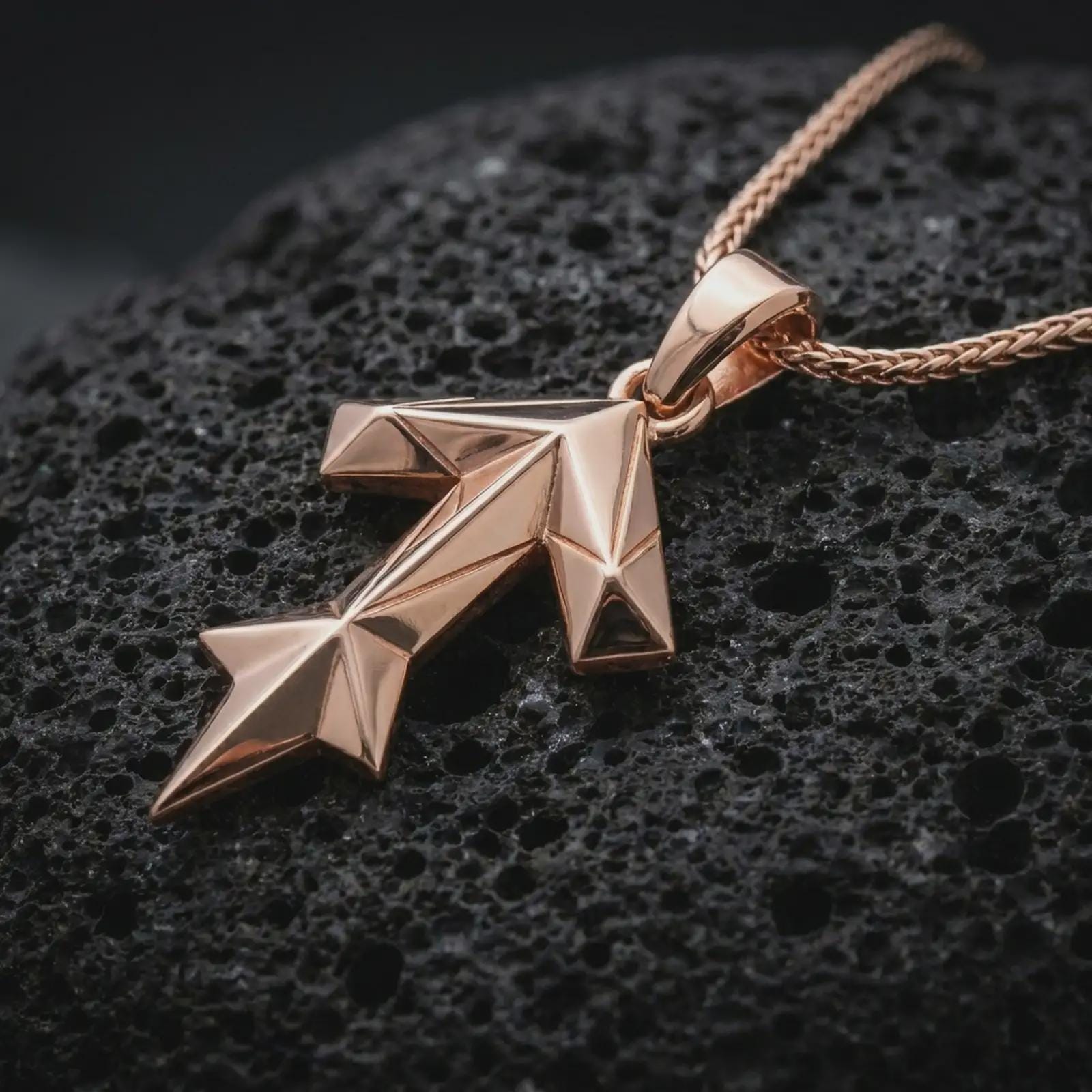 A rose gold plated Tyr rune pendant is photographed on porous volcanic rock in a close-up studio composition with refined luxury lighting and faceted sculptural detail.