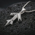 Load image into Gallery viewer, A polished silver Tyr rune pendant is displayed on black volcanic rock in a premium macro studio close-up with sharp angular lines and clean symbolic detail.
