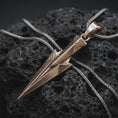 Load image into Gallery viewer, A bronze Gungnir pendant rests on dark volcanic rock in a macro studio close-up, showing Odin’s spear in a sharp geometric Norse design.
