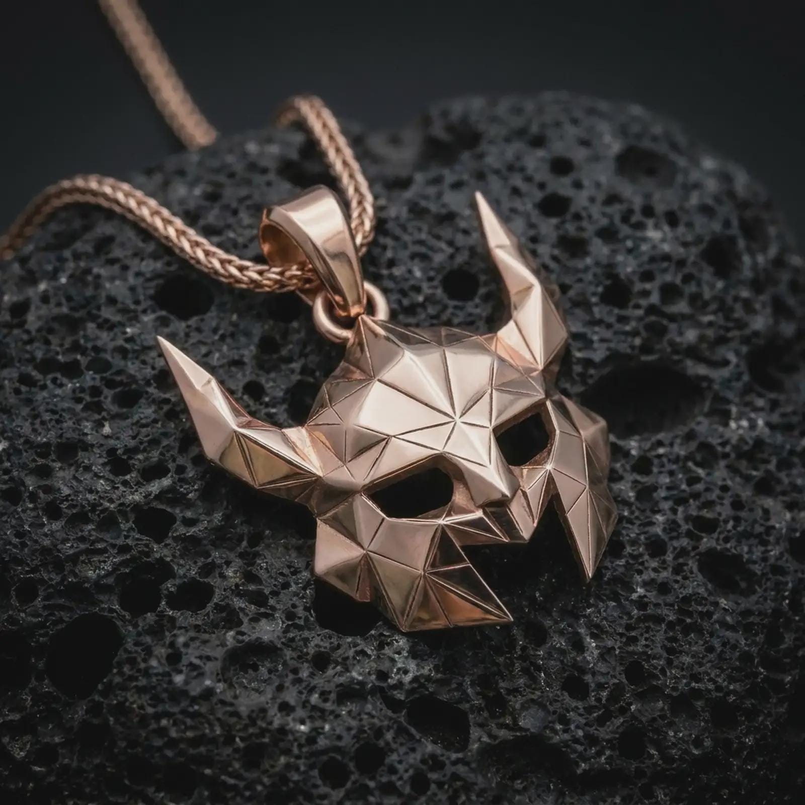 A rose gold plated Helm of Awe inspired mask pendant is photographed on porous volcanic rock in a close-up studio composition with bold luxury lighting.