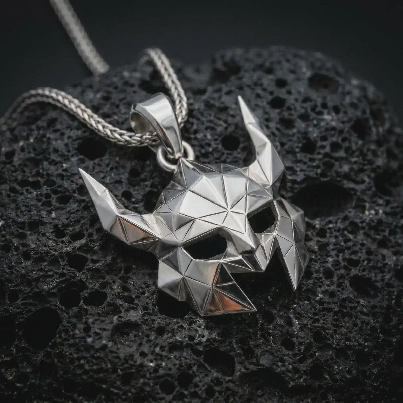 A polished silver Helm of Awe inspired mask pendant is displayed on black volcanic rock in a premium macro studio close-up with sharp geometric details.