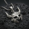 Load image into Gallery viewer, An oxidized Helm of Awe inspired mask pendant rests on dark volcanic rock in a macro studio close-up, showing a faceted horned Norse warrior design.
